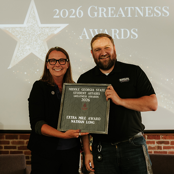 Dr. Jennifer Brannon and award recipient Nathan Long smile while holding a plaque that reads, "Middle Georgia State Student Affairs Greatness Awards 2026 - Extra Mile Award, Nathan Long."
